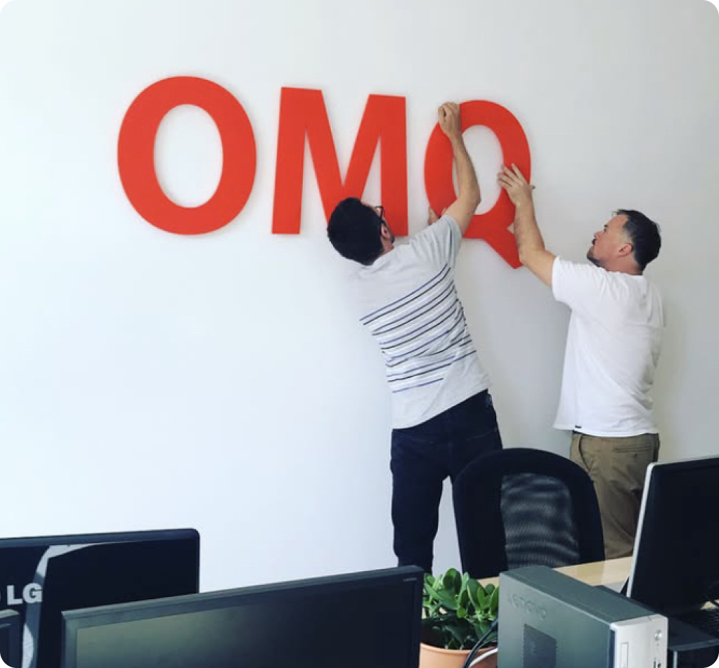 Matthias und Sven befestigen das OMQ Logo im Office an der Wand